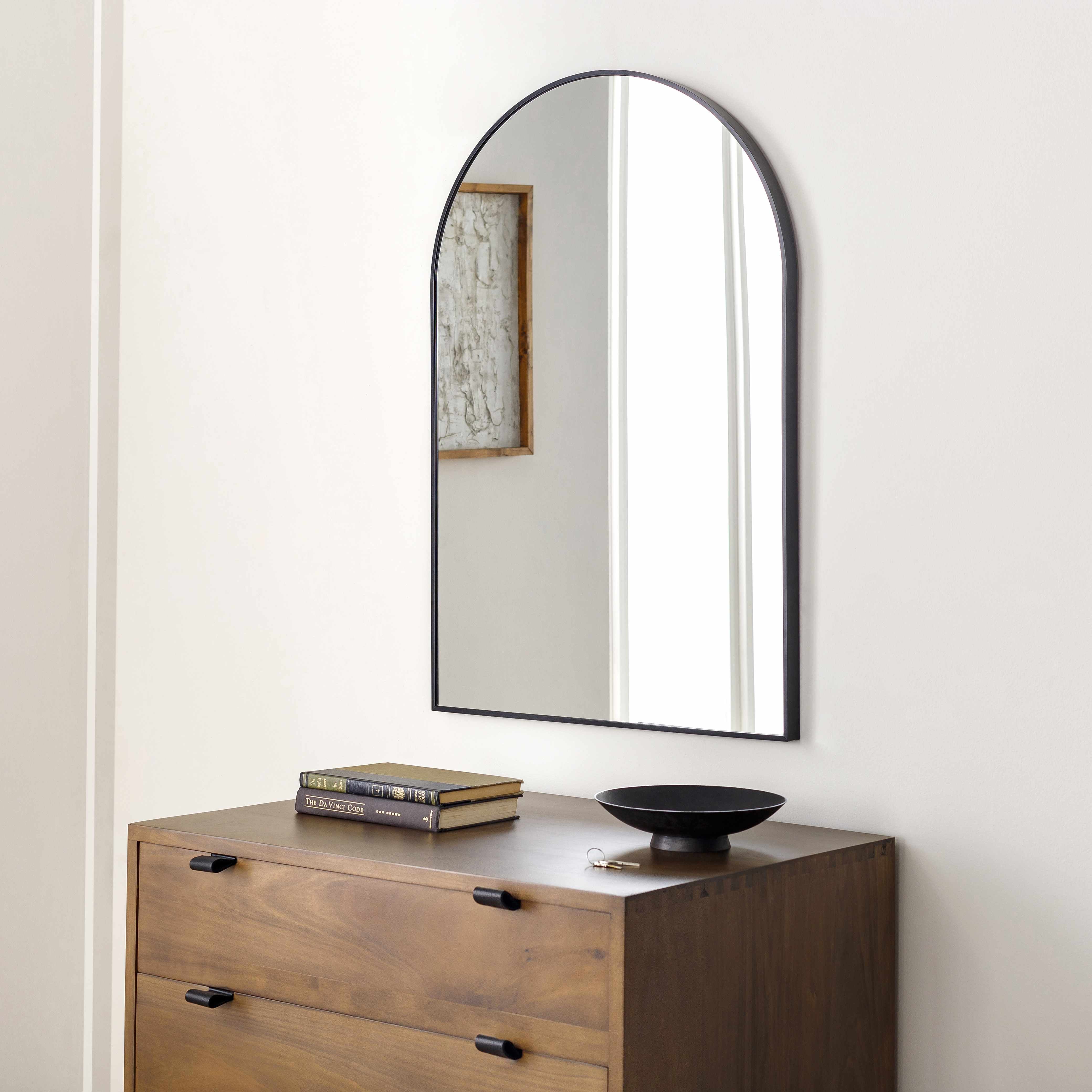 Wooden dresser with a large arched mirror above it on a white wall.