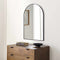 Wooden dresser with a large arched mirror above it on a white wall.